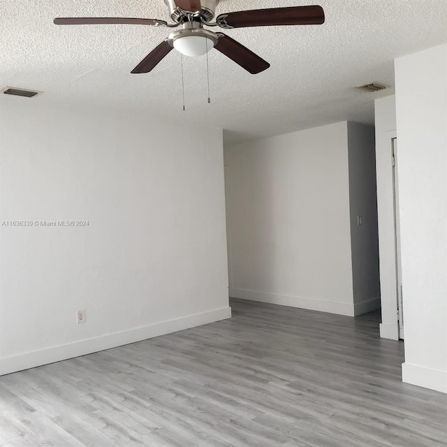 unfurnished room with visible vents, a textured ceiling, baseboards, and wood finished floors