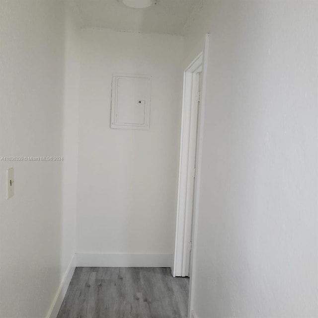 corridor with light wood-style flooring, electric panel, and baseboards