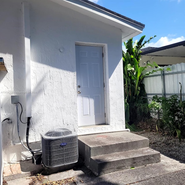 property entrance featuring stucco siding, fence, and central AC unit