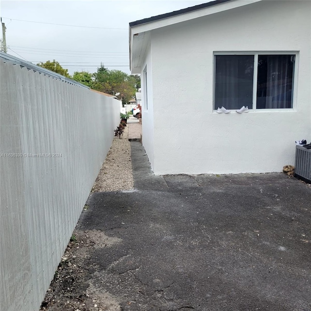 view of side of property with central AC, fence, and stucco siding