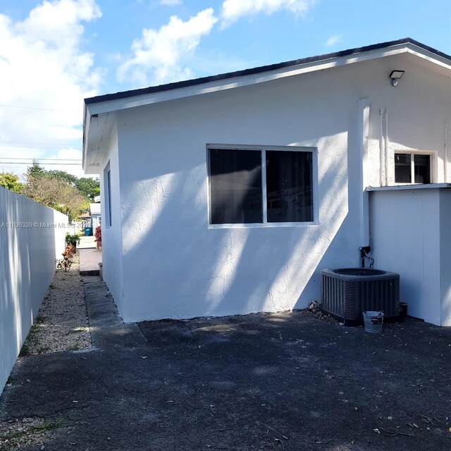 view of side of property featuring fence, central AC unit, and stucco siding