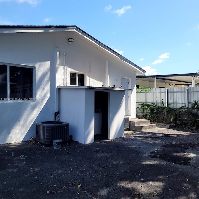 view of side of home with cooling unit, fence, and stucco siding