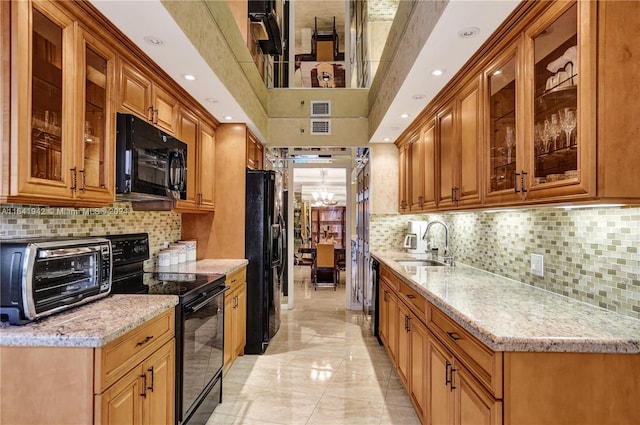 kitchen with light stone countertops, decorative backsplash, black appliances, and sink