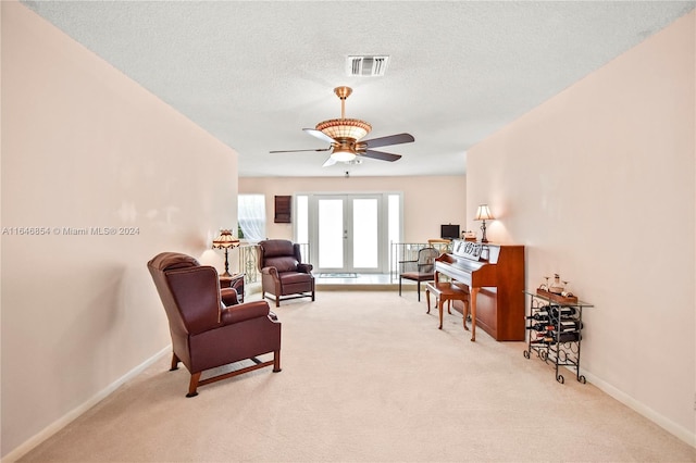 living area featuring ceiling fan, light colored carpet, and a textured ceiling