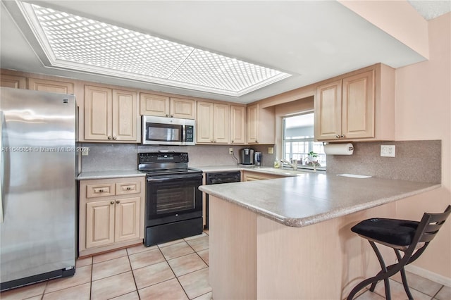 kitchen featuring a breakfast bar, light brown cabinets, appliances with stainless steel finishes, light tile patterned flooring, and kitchen peninsula