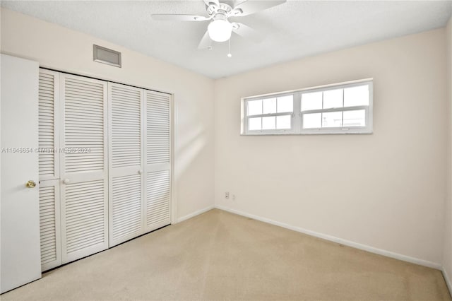 unfurnished bedroom featuring ceiling fan, a closet, light carpet, and a textured ceiling