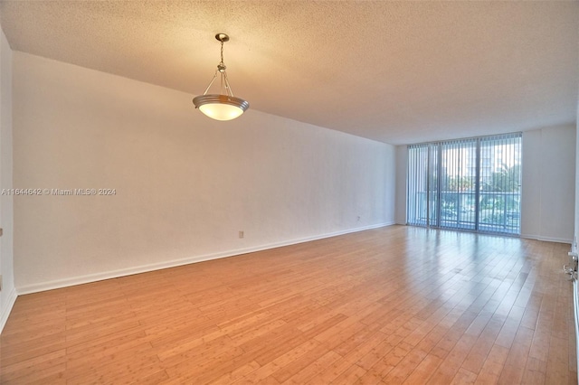 spare room with a wall of windows, a textured ceiling, and light hardwood / wood-style floors