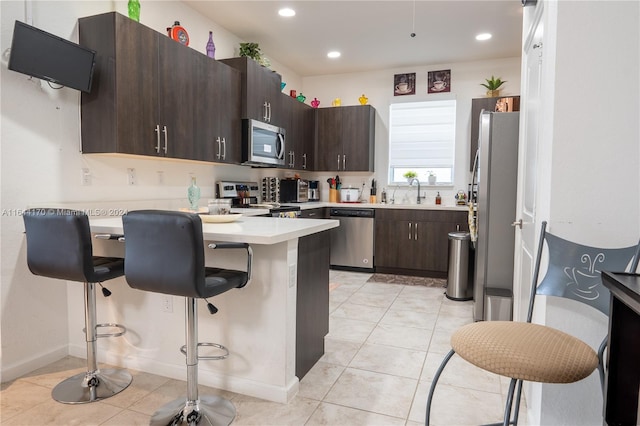 kitchen featuring a kitchen breakfast bar, dark brown cabinets, stainless steel appliances, sink, and light tile patterned floors