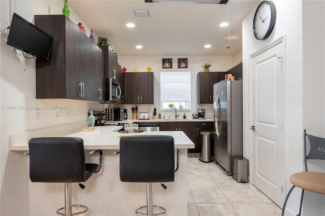 kitchen featuring a kitchen bar, appliances with stainless steel finishes, kitchen peninsula, dark brown cabinetry, and sink