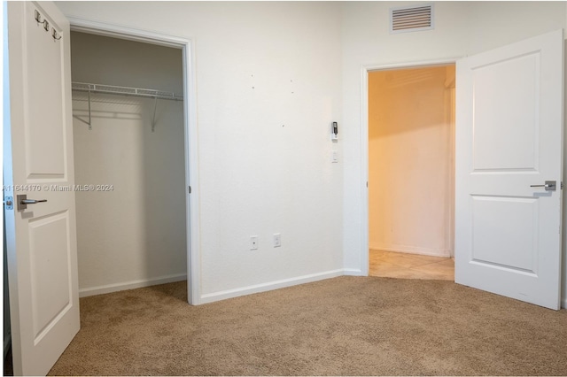 unfurnished bedroom with light colored carpet and a closet