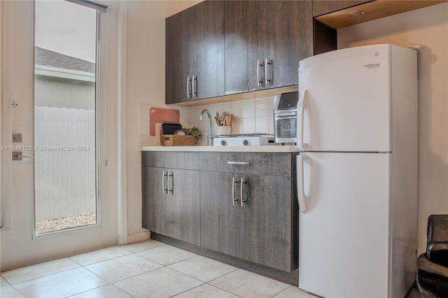 kitchen featuring white fridge, dark brown cabinetry, light tile patterned floors, and tasteful backsplash