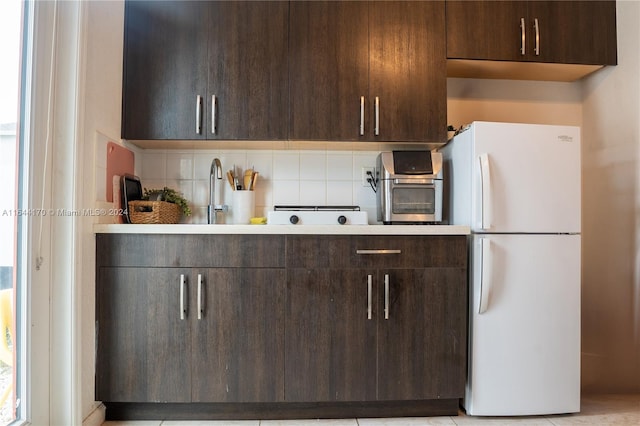 kitchen featuring sink, light tile patterned floors, tasteful backsplash, dark brown cabinets, and white fridge