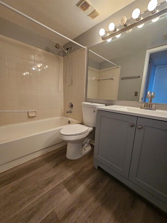 full bathroom with tiled shower / bath combo, vanity, hardwood / wood-style floors, and toilet