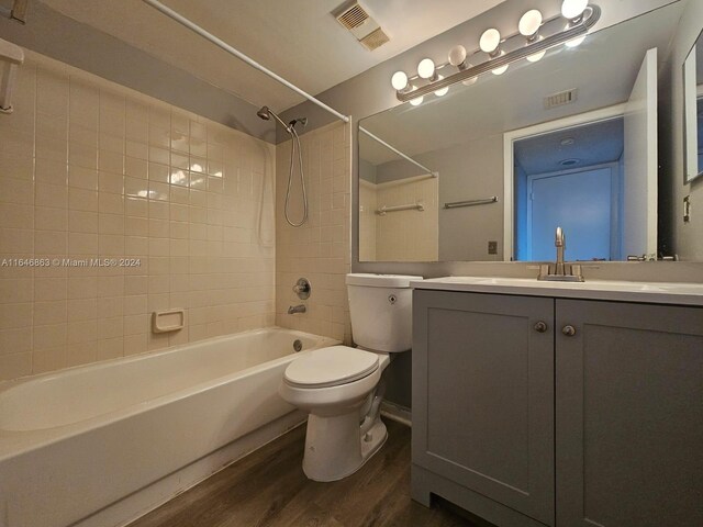 full bathroom with hardwood / wood-style flooring, tiled shower / bath, vanity, and toilet