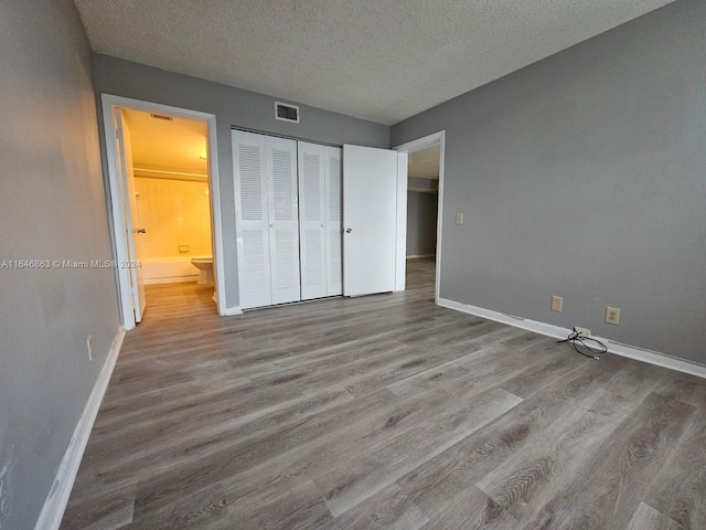 unfurnished bedroom featuring a textured ceiling, a closet, wood-type flooring, and ensuite bathroom