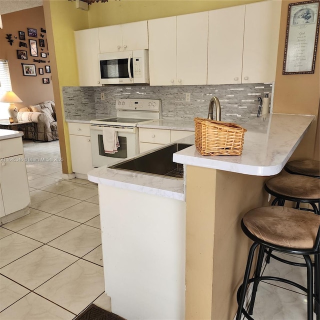 kitchen with a breakfast bar, white appliances, kitchen peninsula, and white cabinets