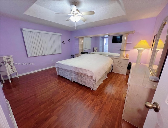 bedroom featuring a textured ceiling, ceiling fan, a tray ceiling, and dark hardwood / wood-style floors