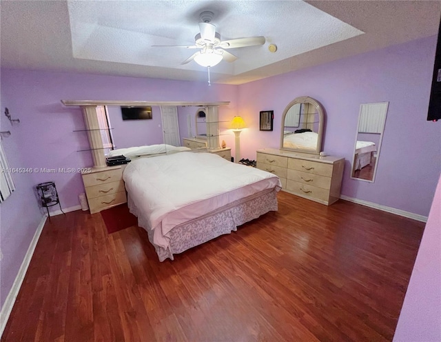 bedroom featuring a tray ceiling, ceiling fan, dark hardwood / wood-style floors, and a textured ceiling