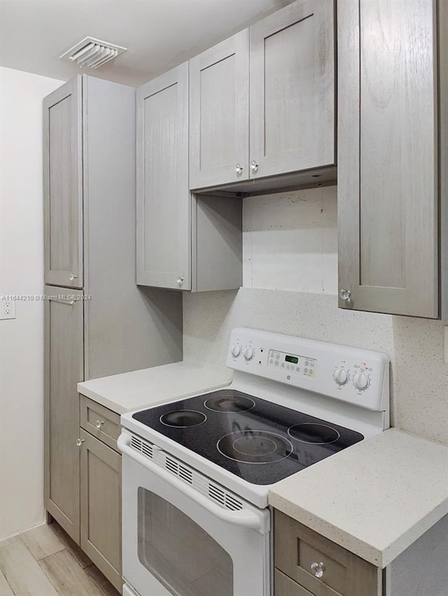 kitchen with gray cabinetry, white electric range, light wood-type flooring, and decorative backsplash