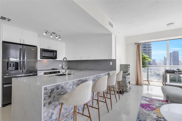 kitchen with stainless steel refrigerator with ice dispenser, backsplash, sink, white cabinets, and a breakfast bar area