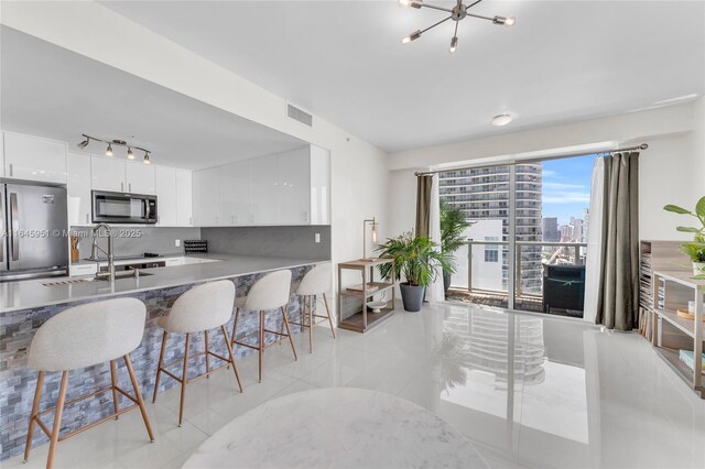 kitchen with freestanding refrigerator, tasteful backsplash, white cabinets, visible vents, and a breakfast bar area