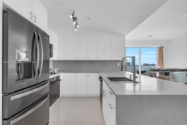 kitchen with a peninsula, a sink, black appliances, white cabinets, and light countertops