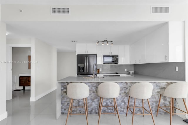 kitchen featuring decorative backsplash, visible vents, stainless steel fridge, and black microwave