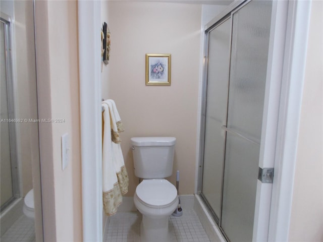 bathroom featuring tile patterned flooring, toilet, and a shower with shower door