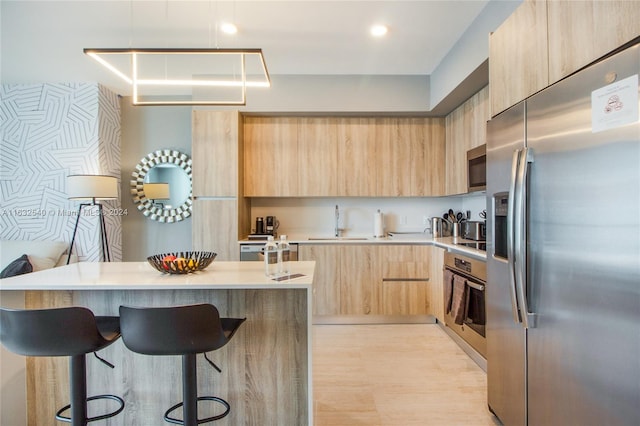 kitchen with light brown cabinets, a kitchen breakfast bar, light hardwood / wood-style flooring, sink, and stainless steel appliances