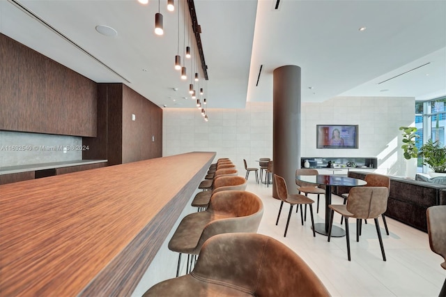 kitchen with light tile patterned floors, a kitchen breakfast bar, pendant lighting, and tile walls