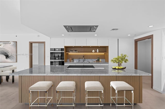 kitchen featuring light stone countertops, a kitchen breakfast bar, sink, black appliances, and white cabinets