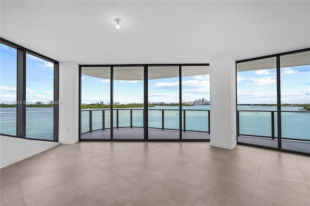 spare room featuring a healthy amount of sunlight, a water view, a wall of windows, and light tile patterned flooring