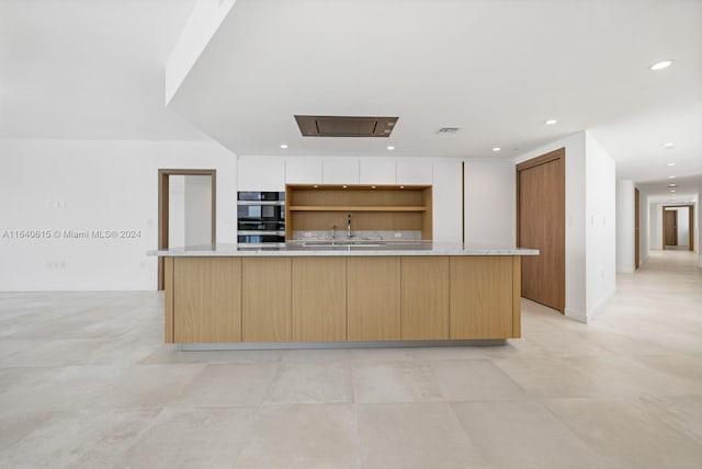 kitchen with sink, stainless steel double oven, white cabinetry, and an island with sink