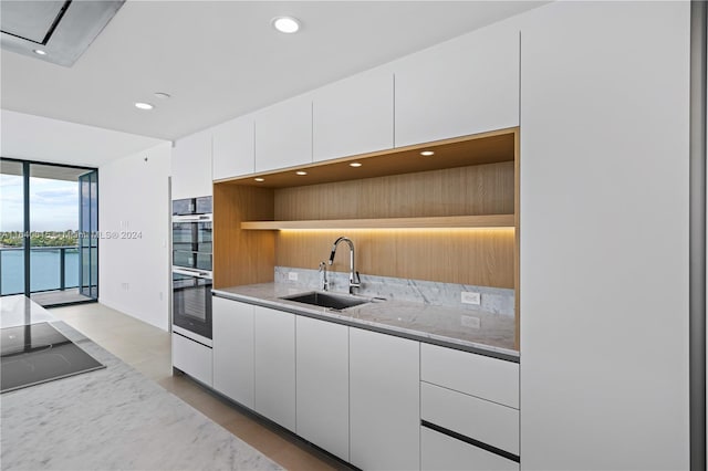 kitchen with light stone countertops, black electric stovetop, sink, a water view, and white cabinets