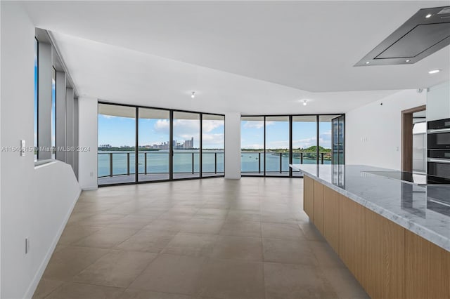 empty room with floor to ceiling windows, plenty of natural light, a water view, and light tile patterned floors