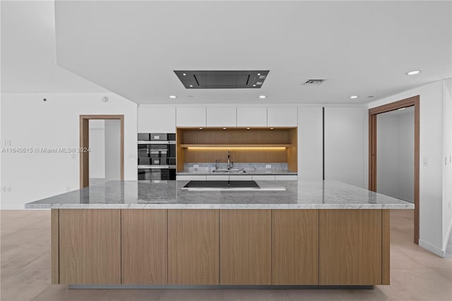 kitchen featuring a spacious island, black appliances, light stone counters, and white cabinets