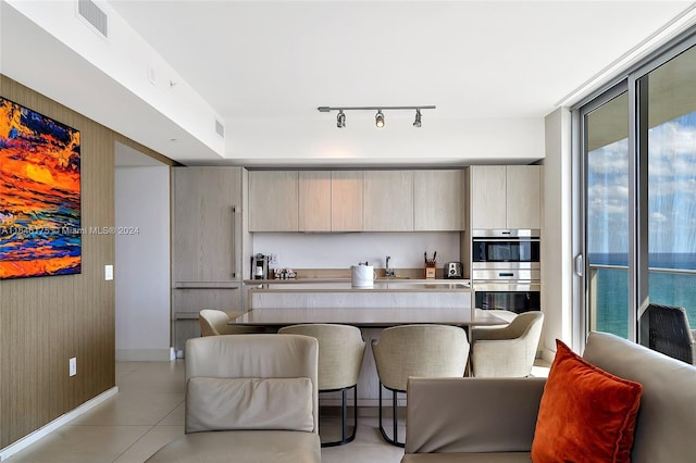 kitchen featuring light tile patterned flooring, stainless steel double oven, light brown cabinetry, a water view, and track lighting