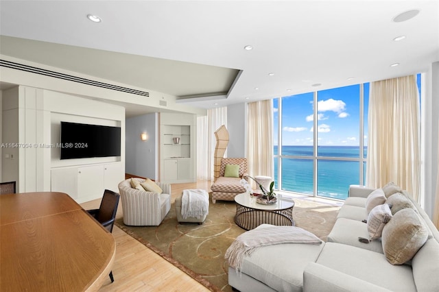 living room with built in shelves, recessed lighting, a water view, wood finished floors, and floor to ceiling windows