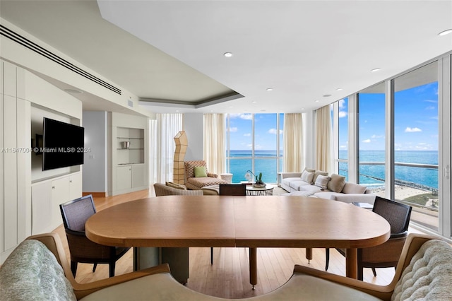 dining space featuring light wood-type flooring, expansive windows, a water view, and built in shelves