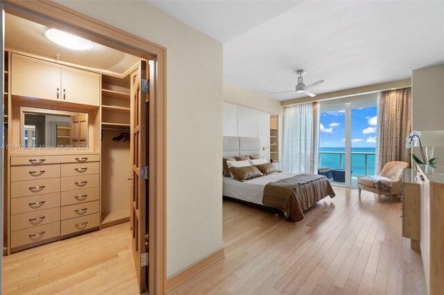 bedroom featuring a walk in closet, light wood-type flooring, a water view, access to exterior, and ceiling fan