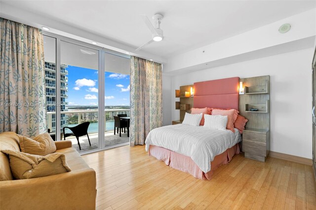 bedroom with a water view, light hardwood / wood-style floors, access to exterior, ceiling fan, and a wall of windows