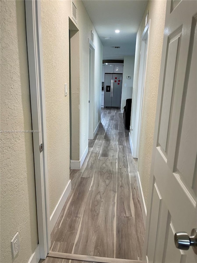 hallway with a textured wall, wood finished floors, visible vents, and baseboards