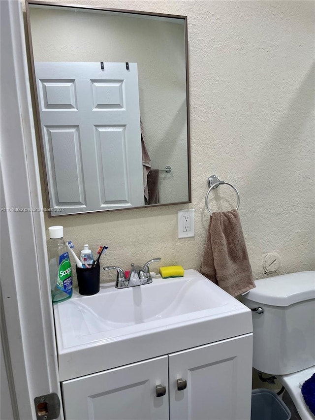 half bath featuring toilet, a textured wall, and vanity