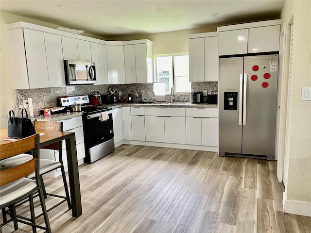 kitchen featuring stainless steel appliances, decorative backsplash, light wood-style floors, white cabinets, and a sink