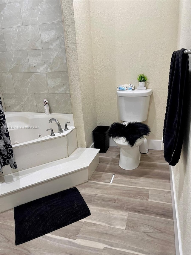 full bathroom featuring a jetted tub, baseboards, toilet, and a textured wall