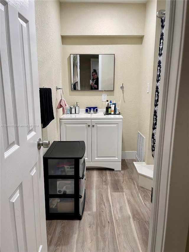 bathroom with baseboards, visible vents, a textured wall, wood finished floors, and vanity