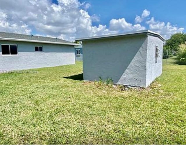 view of side of home featuring a lawn, an outdoor structure, and stucco siding