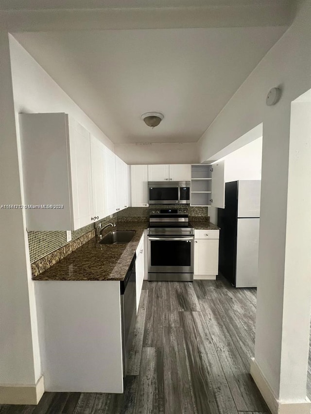 kitchen featuring appliances with stainless steel finishes, sink, white cabinets, wood-type flooring, and dark stone countertops