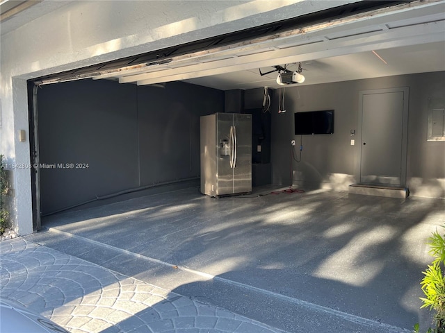 garage featuring a garage door opener and stainless steel refrigerator with ice dispenser