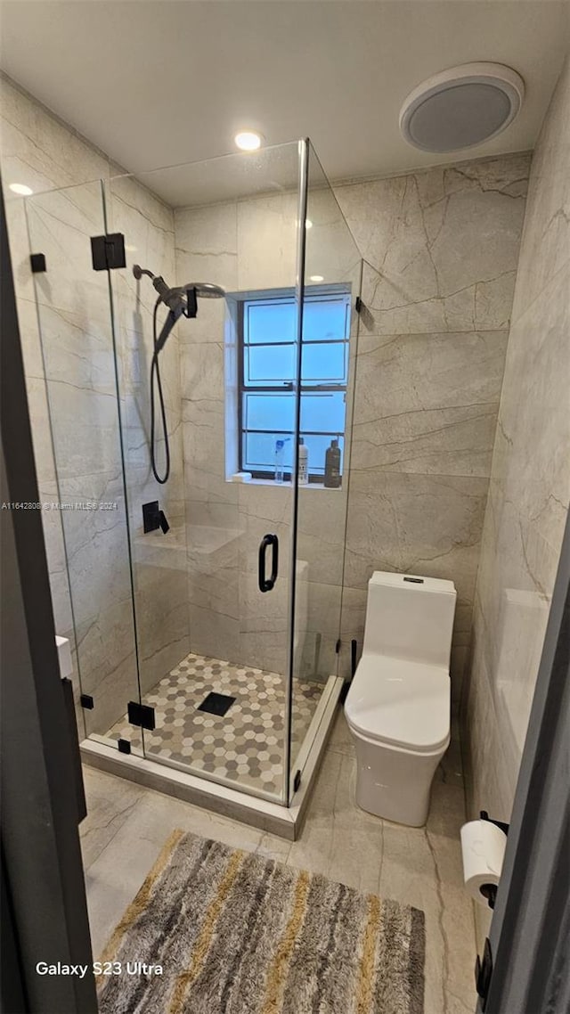 bathroom featuring toilet, tile walls, and a shower with shower door